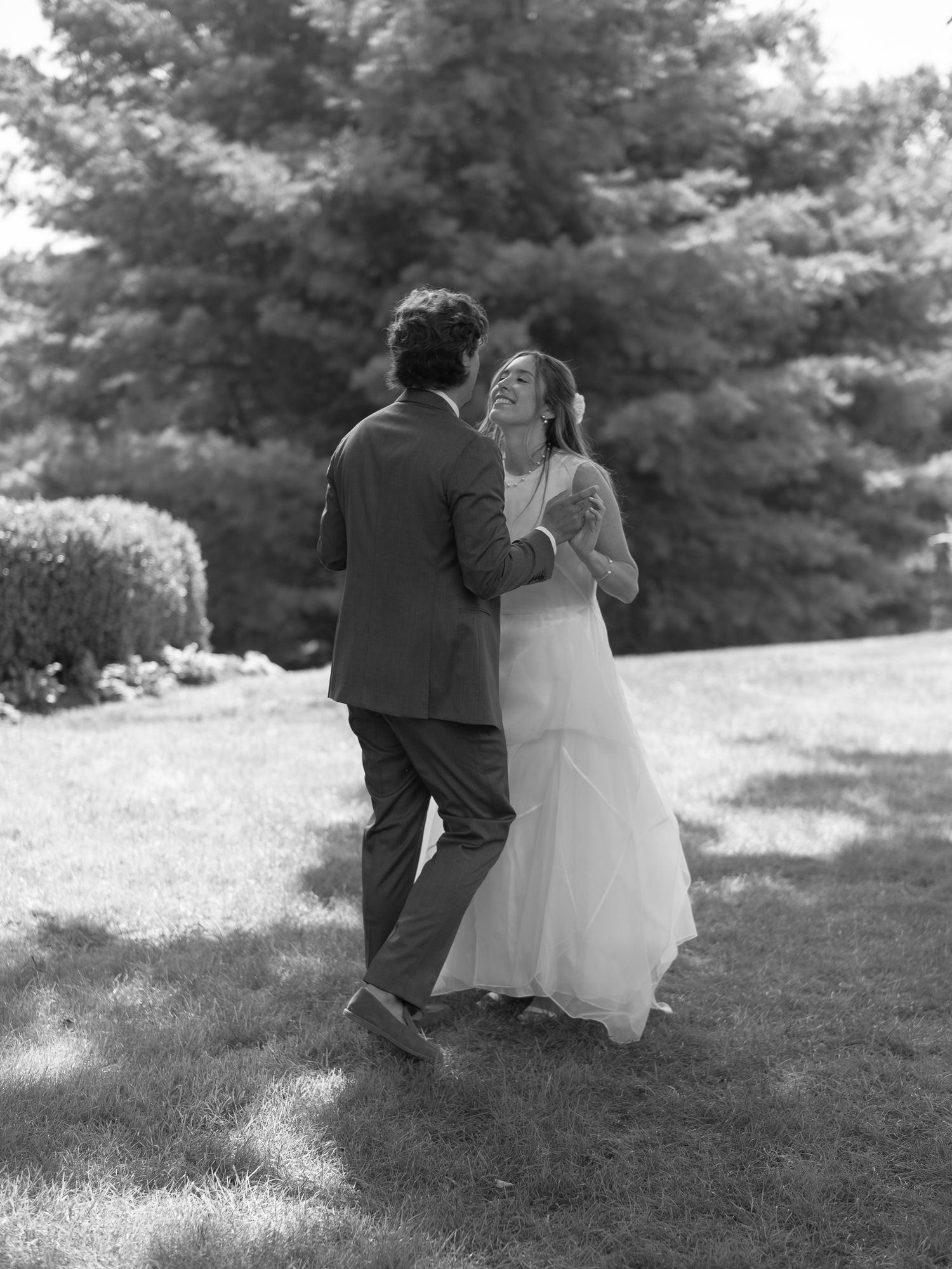 A romantic black and white wedding photo of a couple sitting together on grass surrounded by trees.