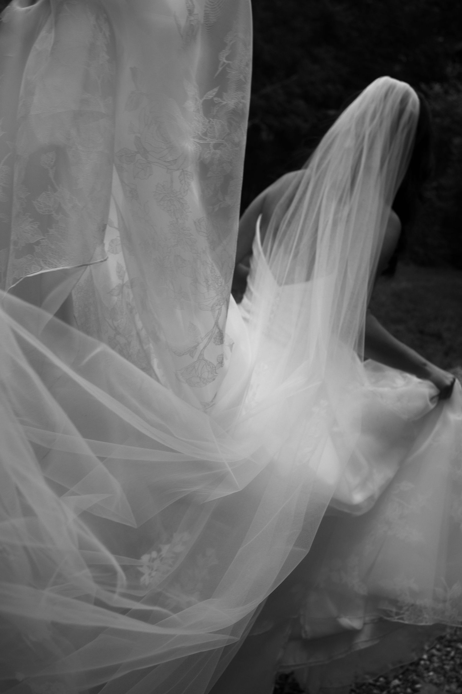Black and white photo of a bride in flowing wedding dress and veil billowing gracefully outdoors.