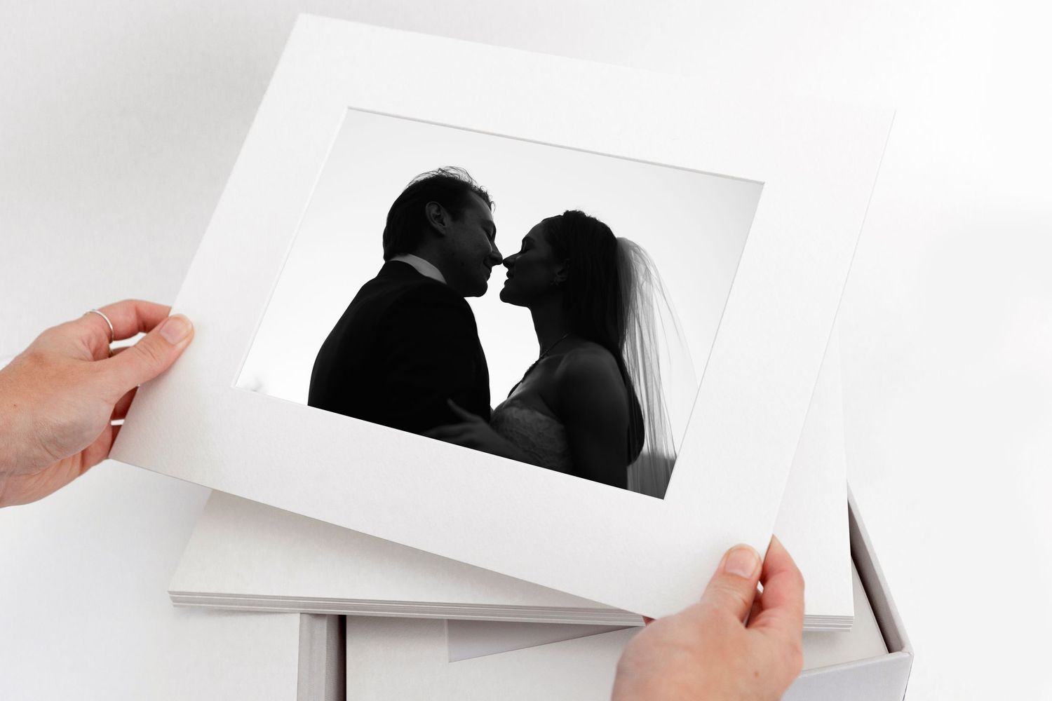 Hands holding a framed black and white wedding photo of a couple kissing, displayed in a white mat board.