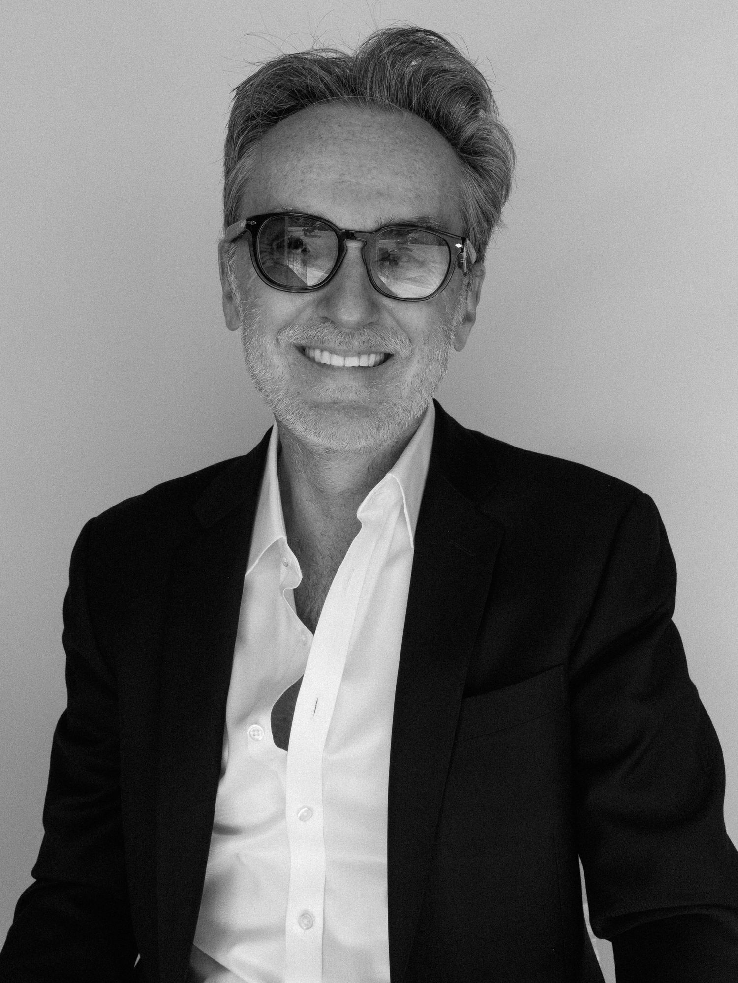 Black and white portrait of a middle-aged man wearing glasses and a blazer, smiling confidently.
