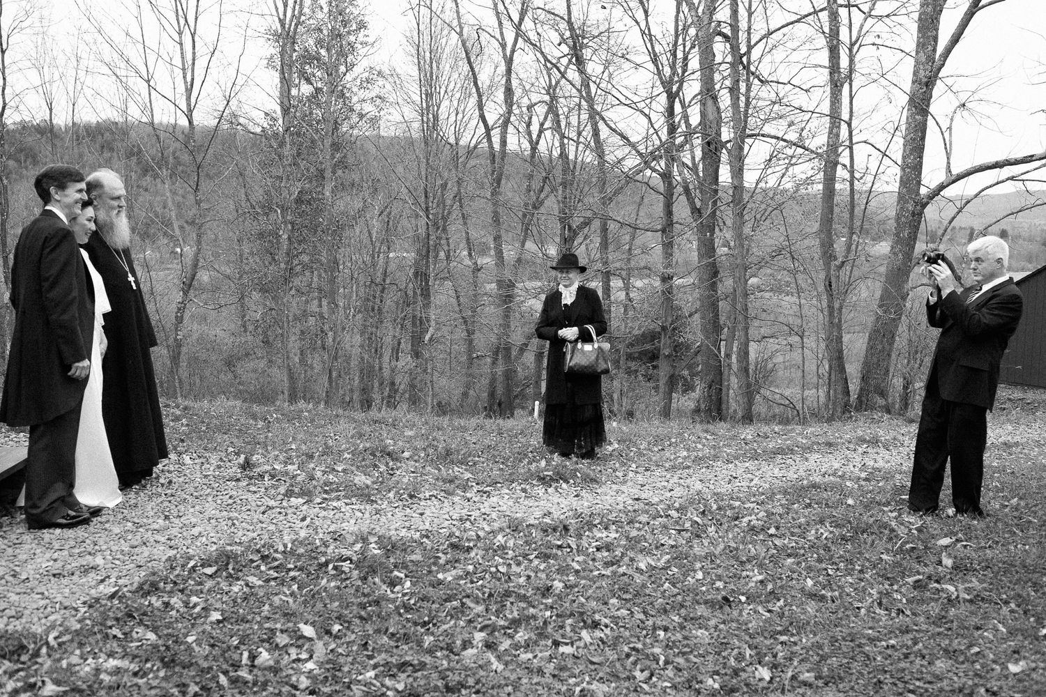 Black and white photo of people in period costumes outdoors, with bare trees and hills in the background.