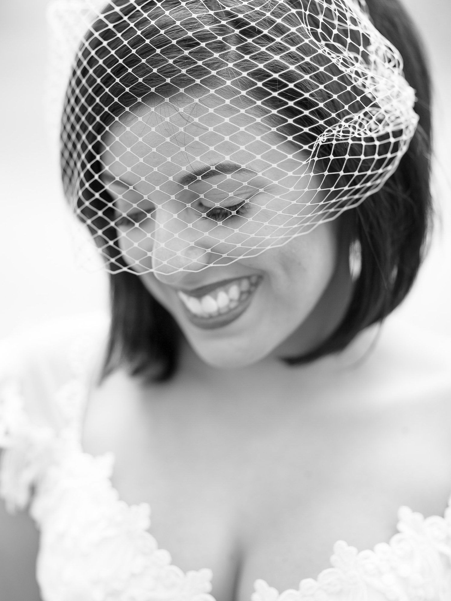 Elegant bride wearing a vintage birdcage veil smiles in classic black and white portrait.