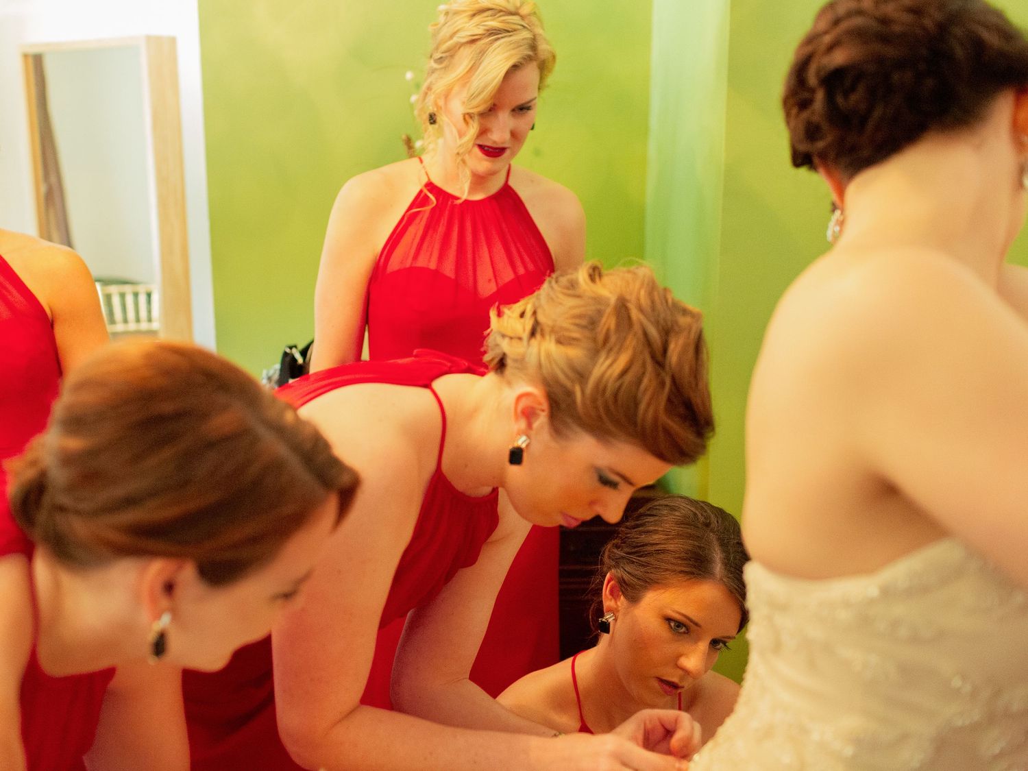 Bridesmaids in red dresses help a bride in a white gown prepare before the wedding ceremony.