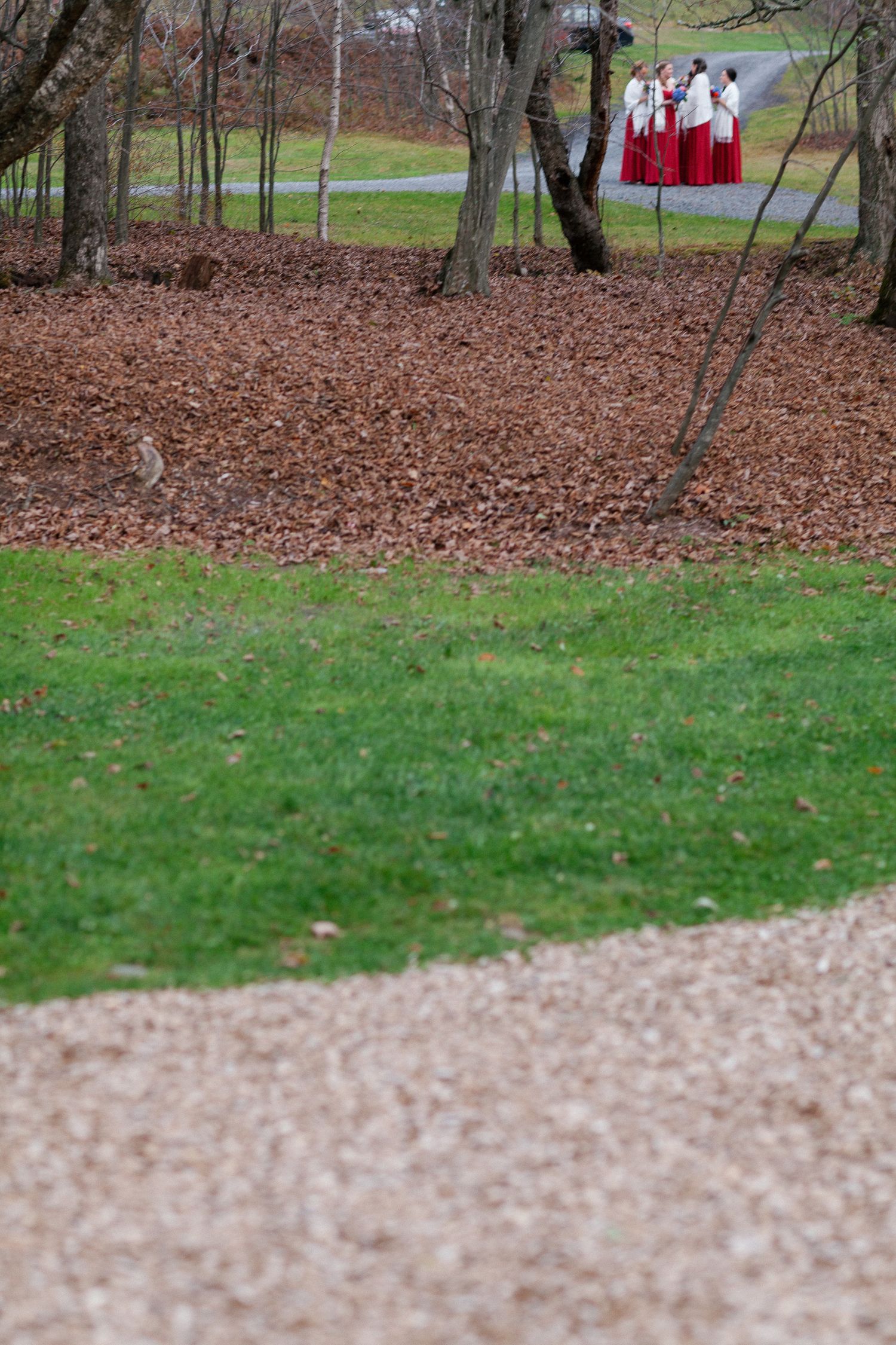 Choir members in red and white robes gather near autumn trees beside a gravel path in a park.