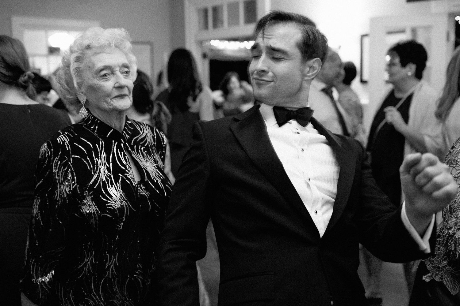 Elderly woman and young man in tuxedo dancing together at a formal black and white event.