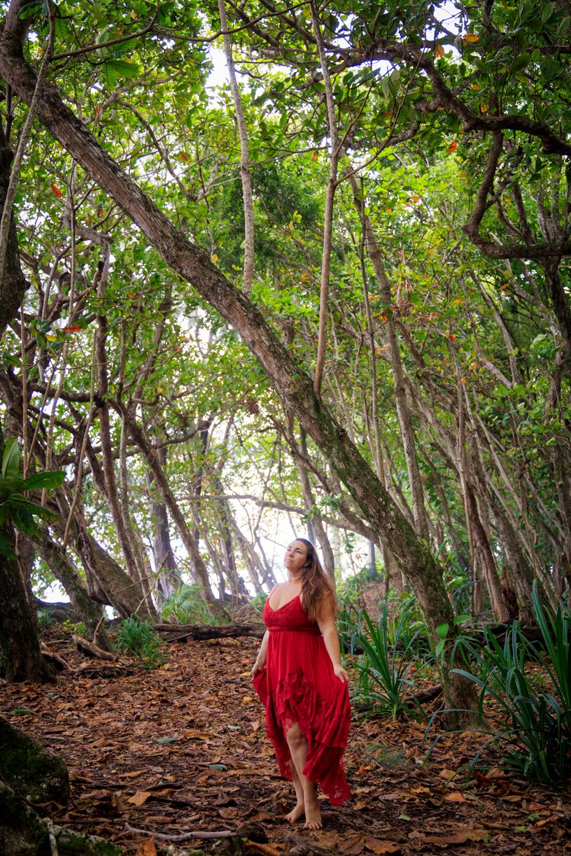 Woman in red dress walking through lush forest with sunlight filtering through trees.
