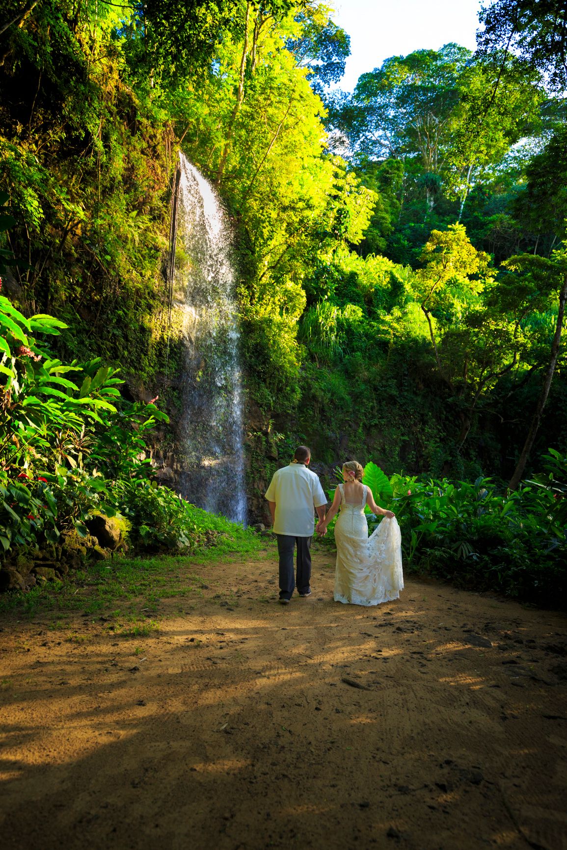Wedding couple walking down a shaded tropical forest path.