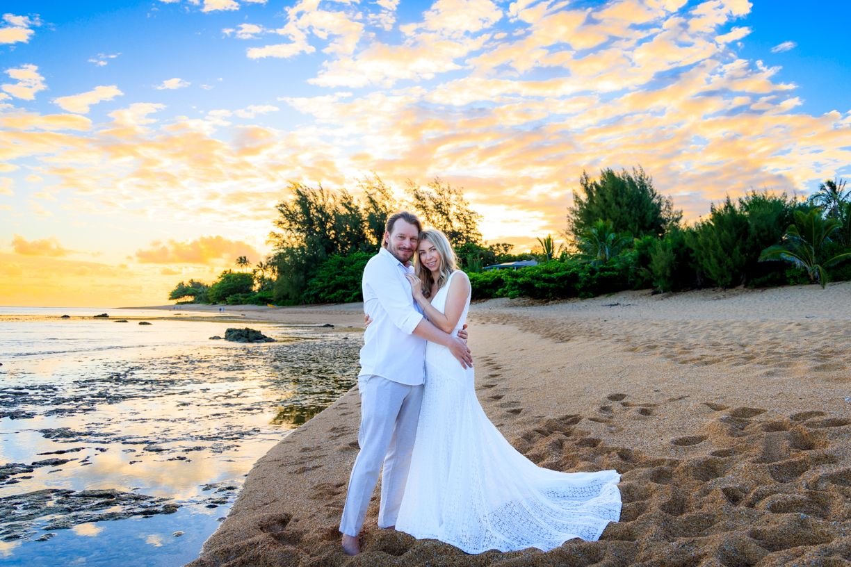 A romantic beach photoshoot at sunset with white sand and dramatic cloud formations.