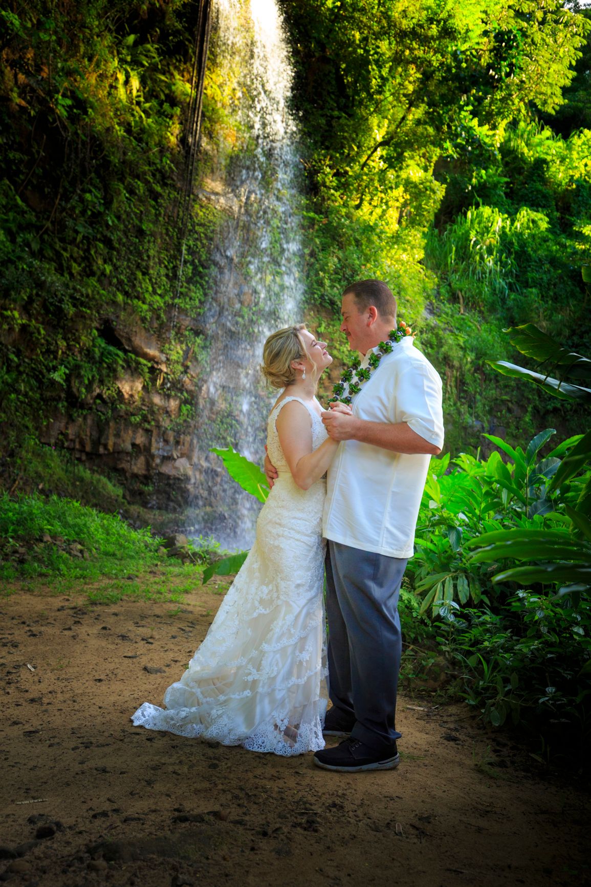 Wedding photography session by tropical waterfall in lush Hawaiian garden setting.