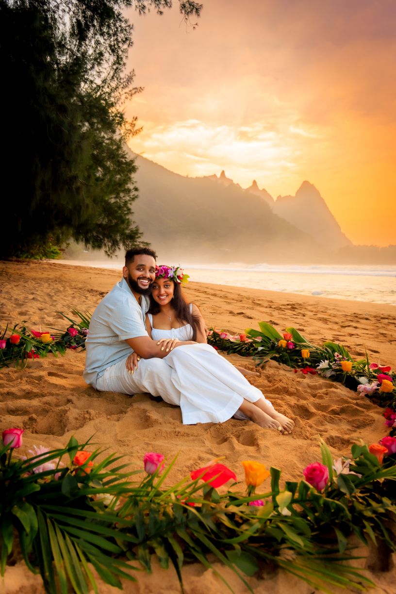 A sunset beach portrait surrounded by colorful tropical flowers with mountains in background.