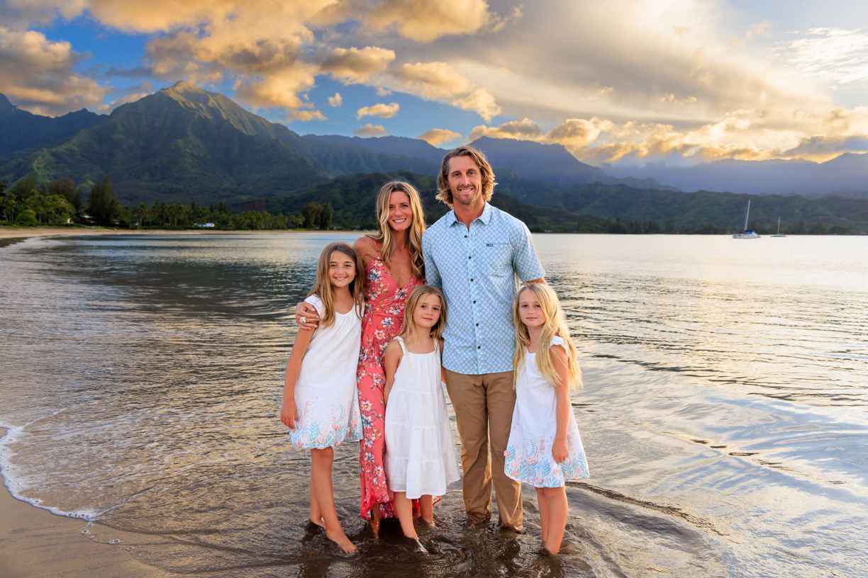 Family dressed in white and blue taking beach portraits at sunset.