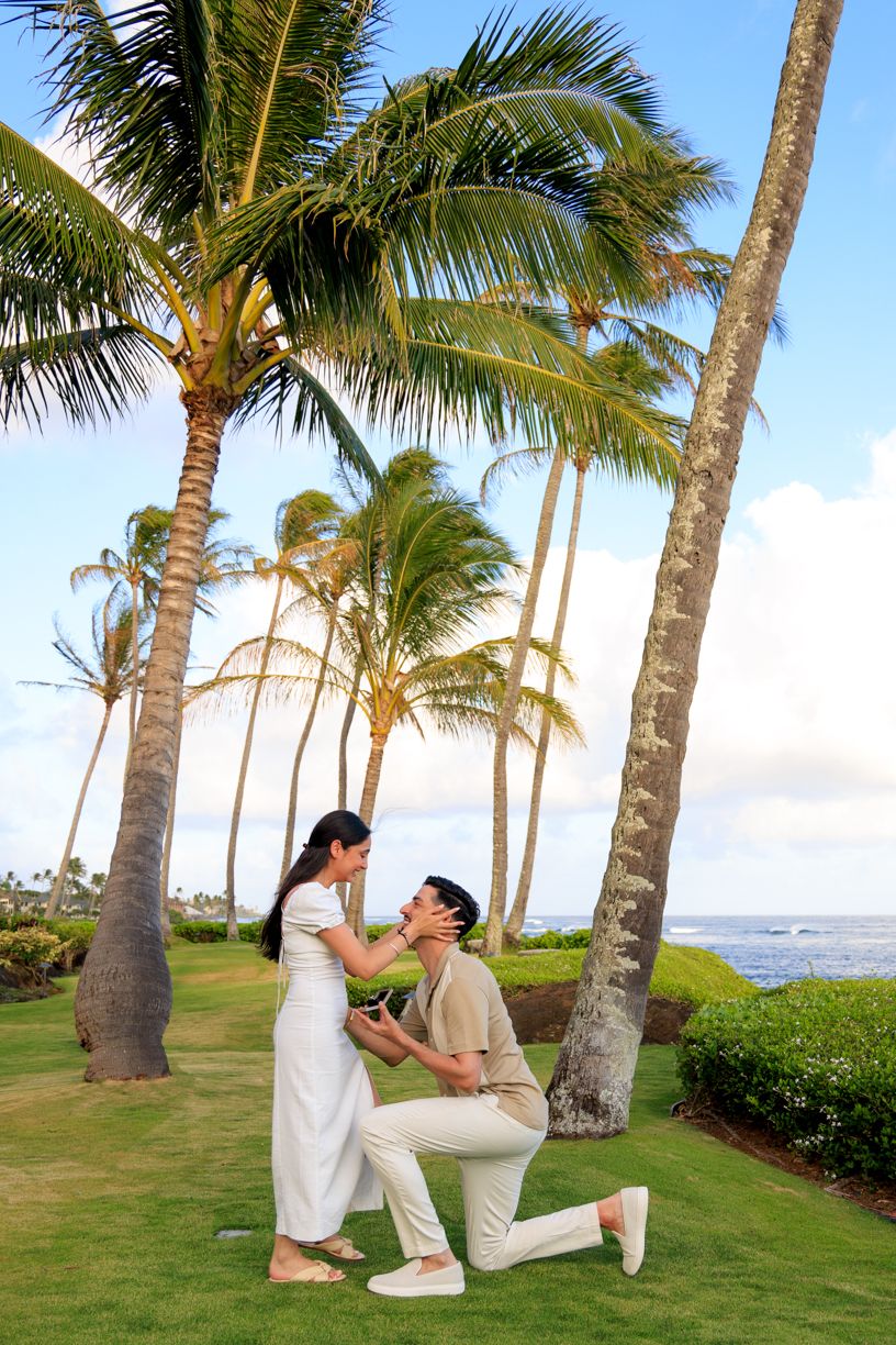 Couple poses under swaying palm trees on a tropical lawn by the ocean.