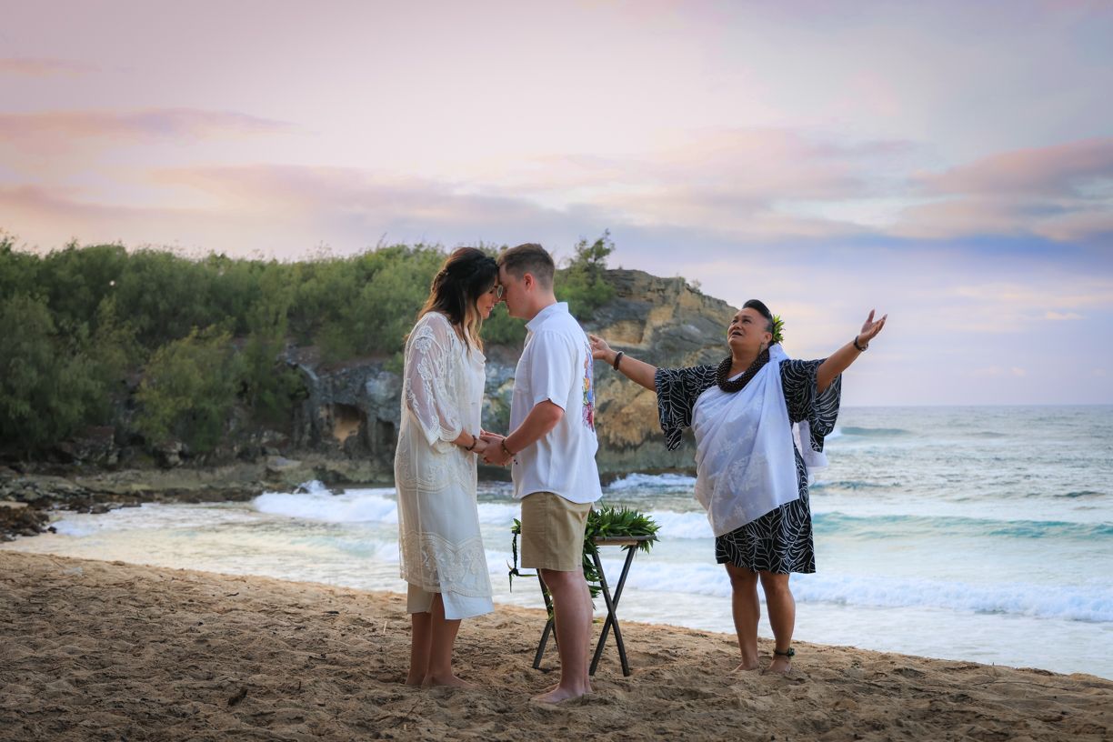 A beach ceremony taking place at sunset with mountains and ocean waves in the background.
