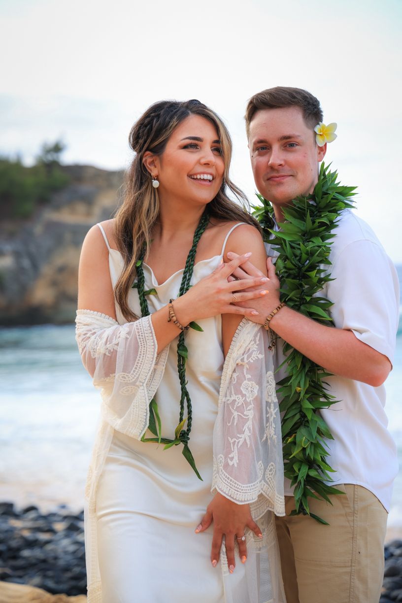 A romantic beach wedding portrait with traditional Hawaiian leis and lace dress details.