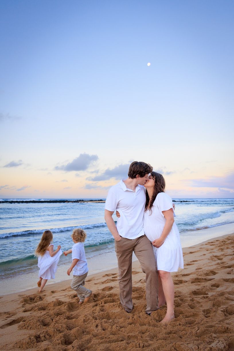 Family walking along sandy beach at sunset with ocean waves in background.