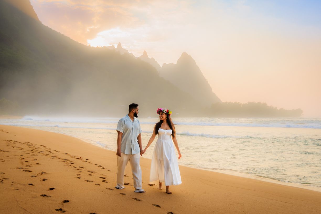 A couple walking hand in hand on a scenic beach with dramatic mountain backdrop at sunset.