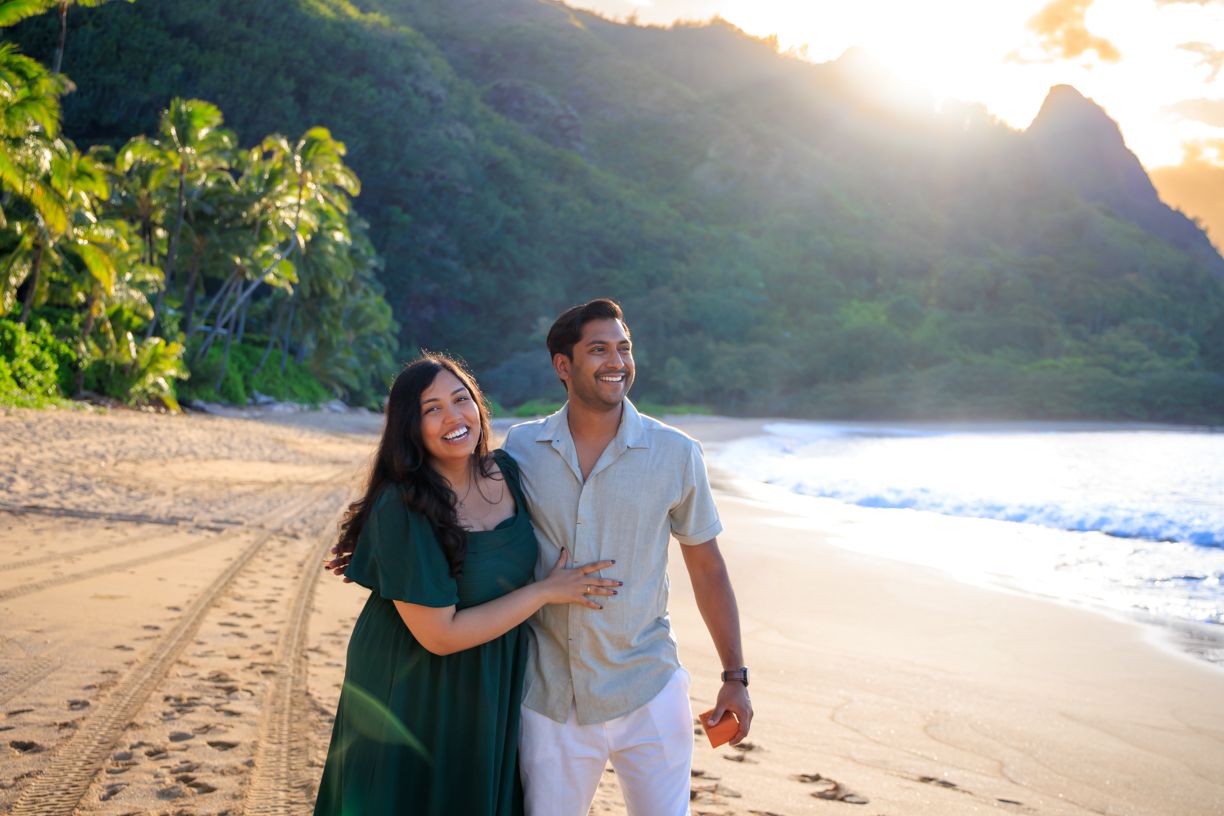 A couple enjoys playful moments on a scenic Hawaiian beach at sunset.