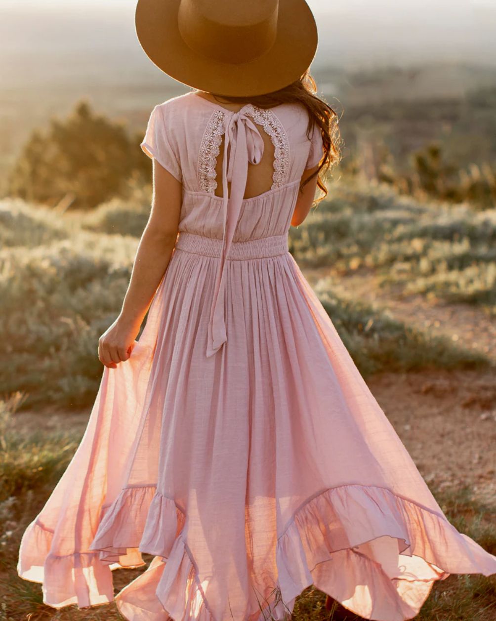 Soft pink prairie dress with ruffled details photographed at sunset in desert landscape.