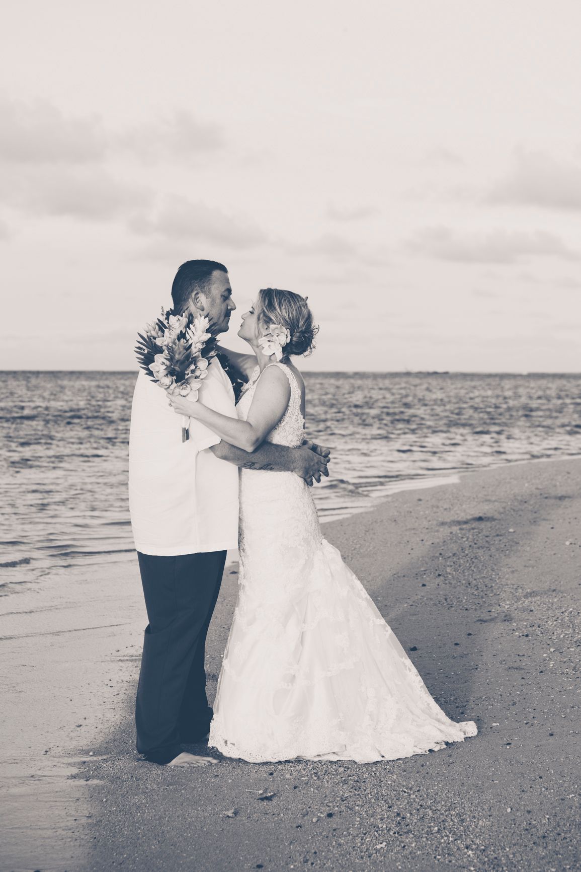 A romantic black and white beach wedding photo of a couple embracing at sunset.