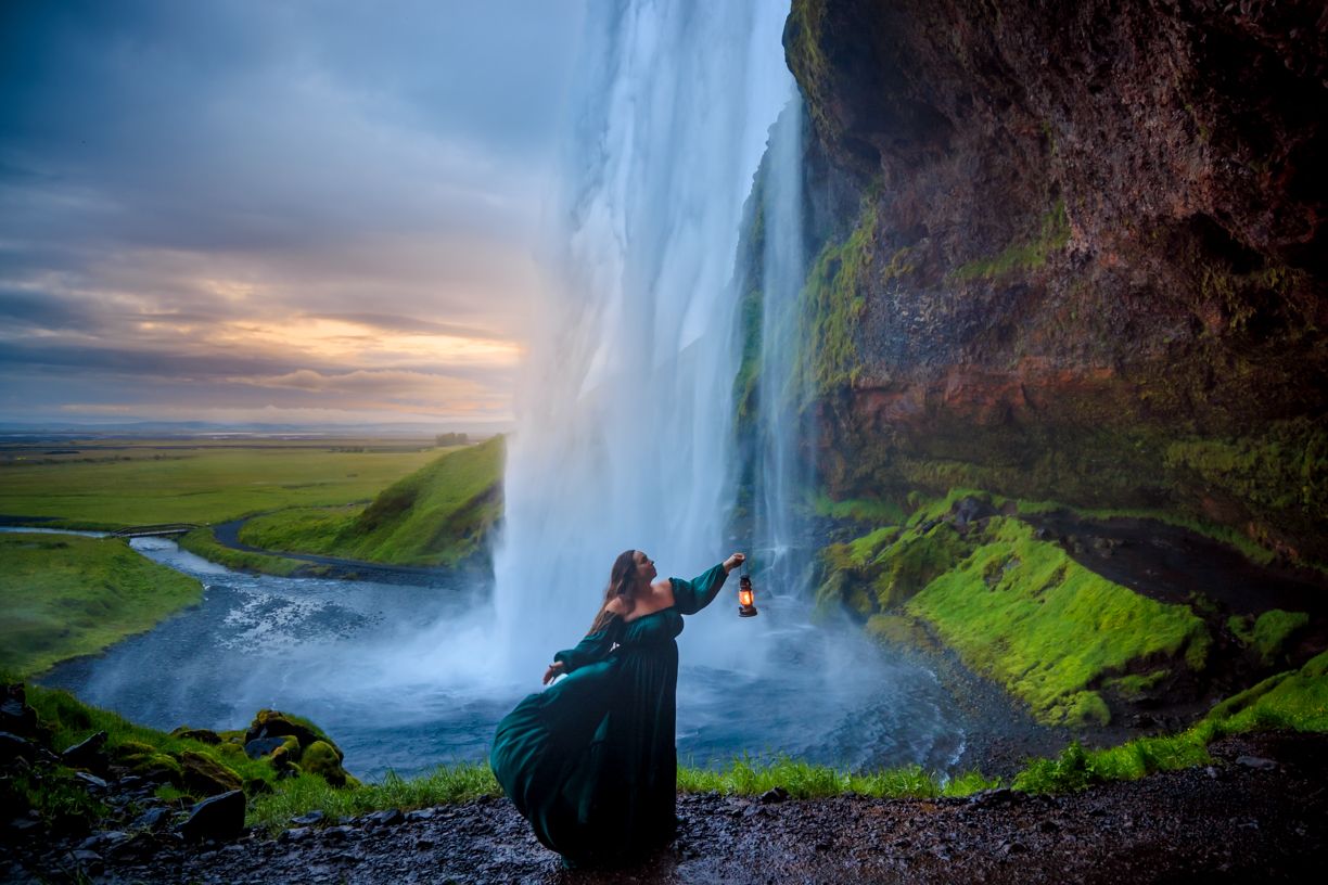 A silhouette stands beneath a massive waterfall against a dramatic sunset sky in Iceland.