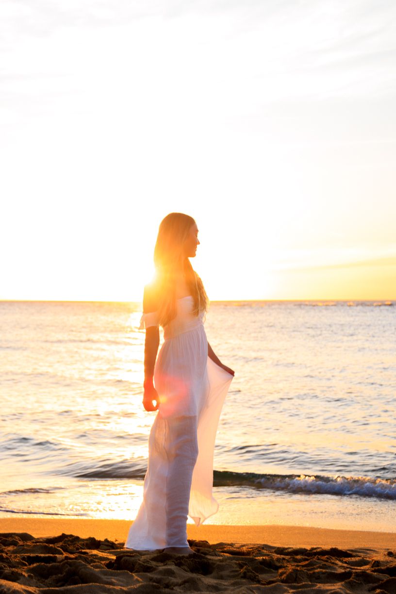 Silhouette of woman in flowing dress on beach at sunset.
