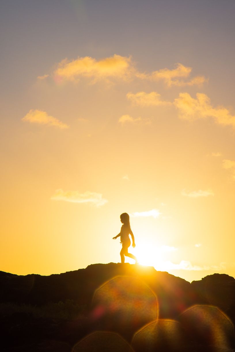 Silhouette of person standing on rock formation at sunset.