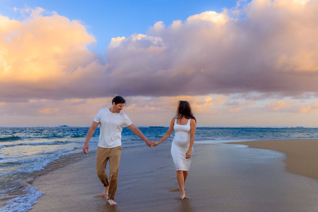 Couple walking along a sunset beach with gentle waves and cloudy sky.