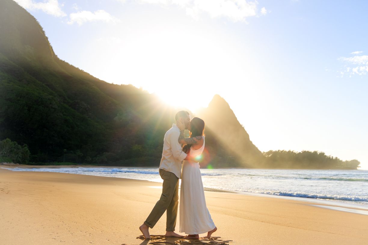 Golden sunset beach scene with mountains and footprints in the sand.
