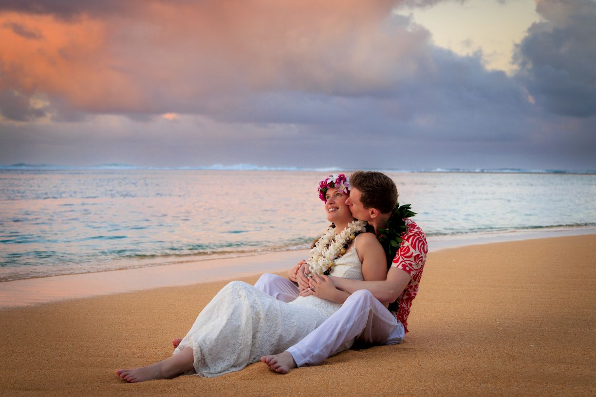 Romantic couple lying on sandy beach at sunset with mountains and ocean in view.