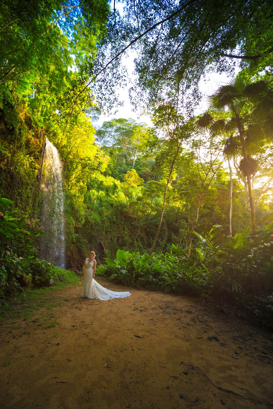 A beautiful wedding photo in a lush tropical forest with a waterfall backdrop.