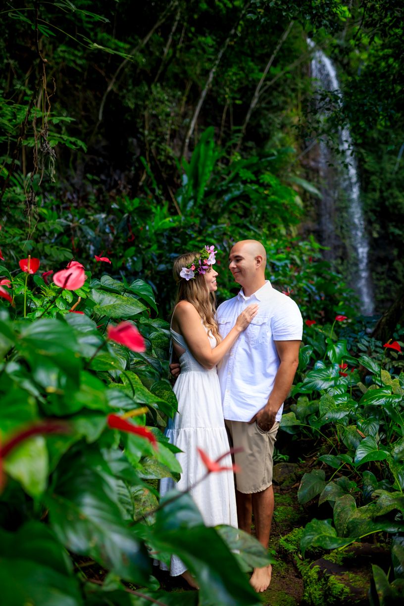 Intimate garden photoshoot among tropical foliage and red anthurium flowers with waterfall backdrop.