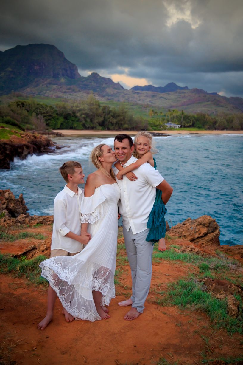 A family poses together on red dirt cliffs overlooking a dramatic Hawaiian coastline.