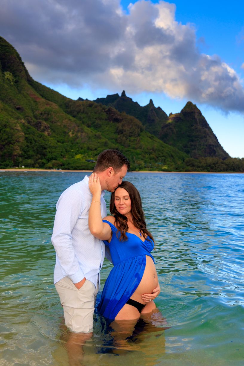 Couple embracing during a romantic beach maternity photoshoot with mountains in the background.