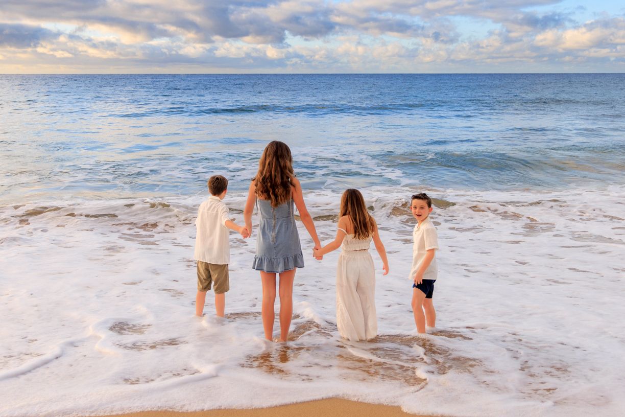 Four people standing at the ocean's edge during sunset watching waves roll in.
