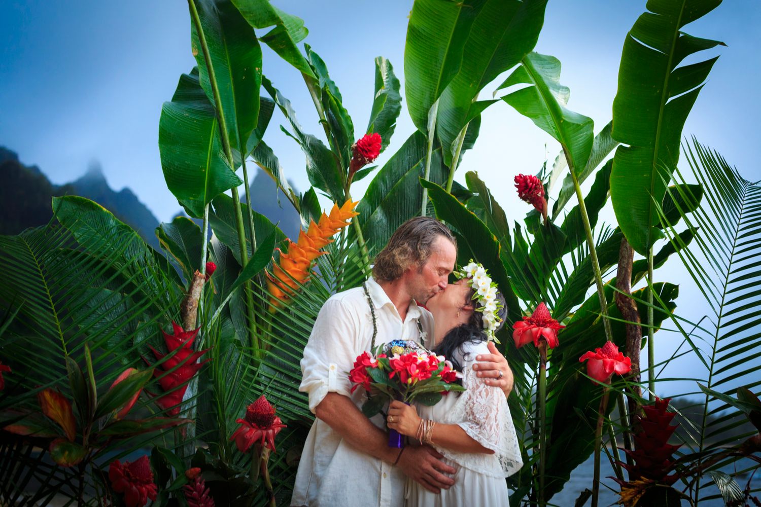 Tropical garden setting with red flowers and palm fronds framing a romantic scene.