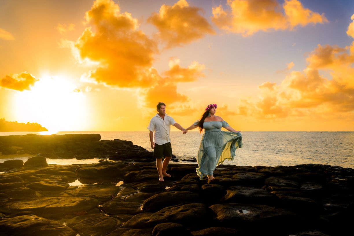 Silhouettes of figures walking along a rocky coastline at sunset with dramatic orange and golden sky at Anini Beach