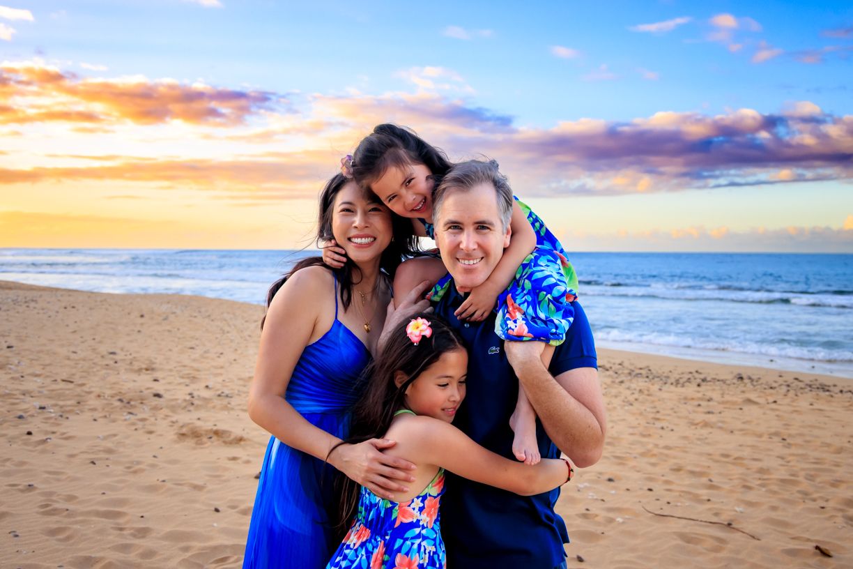 A group embraces on a beach at sunset wearing coordinating blue outfits.