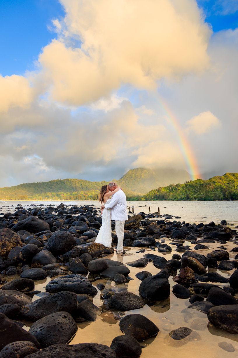 Beautiful rainbow arches over rocky beach coastline during golden hour.