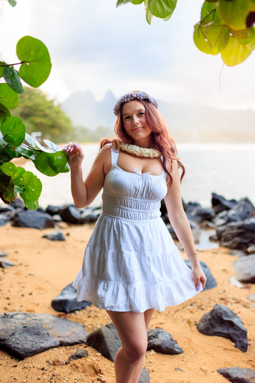 Beachside portrait session with white dress against volcanic rocks and tropical greenery.