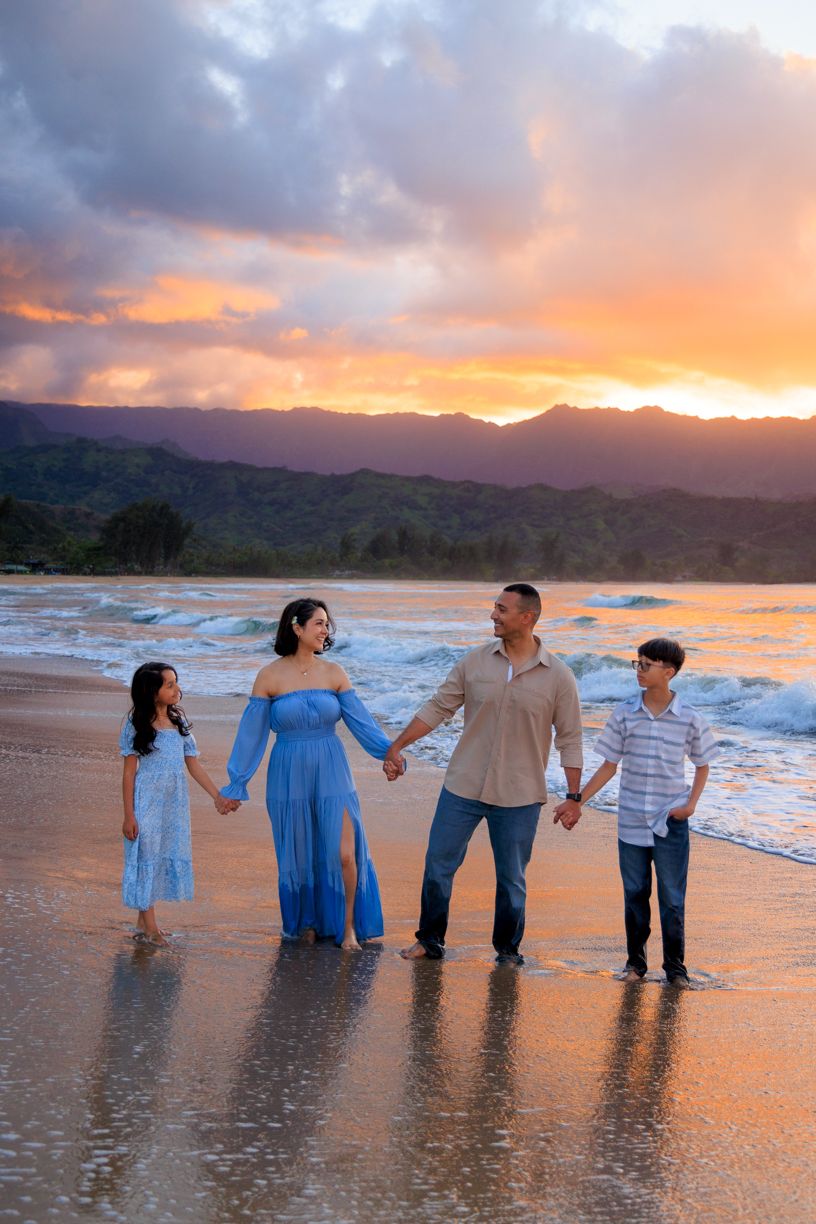 Family wearing coordinated blue outfits standing in ocean water during golden sunset.