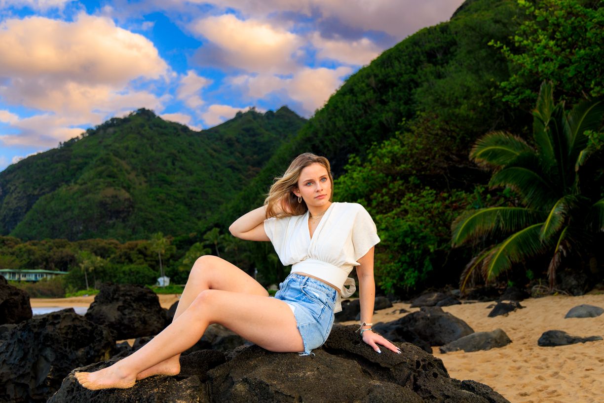 Casual beach portrait on volcanic rocks with lush mountains in background.
