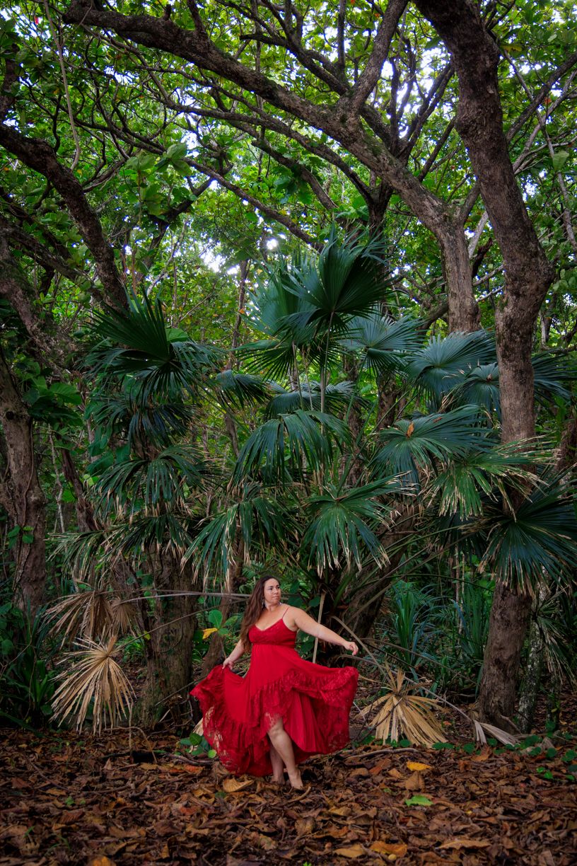 Woman in red dress twirling among lush tropical foliage.