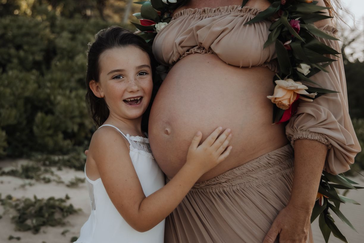 Intimate maternity photos showing a white ruffled dress adorned with red roses and greenery.