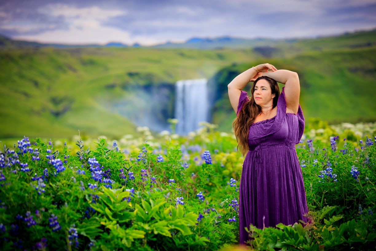 Purple wildflowers bloom in lush green meadow with mountains in background.
