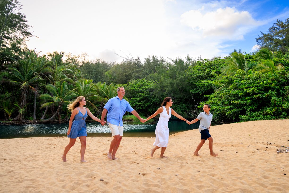 Group holding hands while walking in a line across a tropical beach with lush greenery.