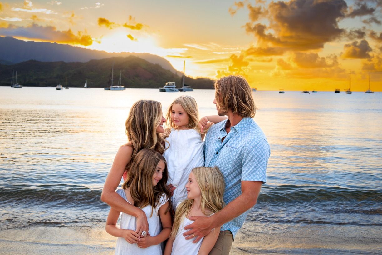 Family portrait session on beach at golden hour with dramatic Hawaiian mountain backdrop.
