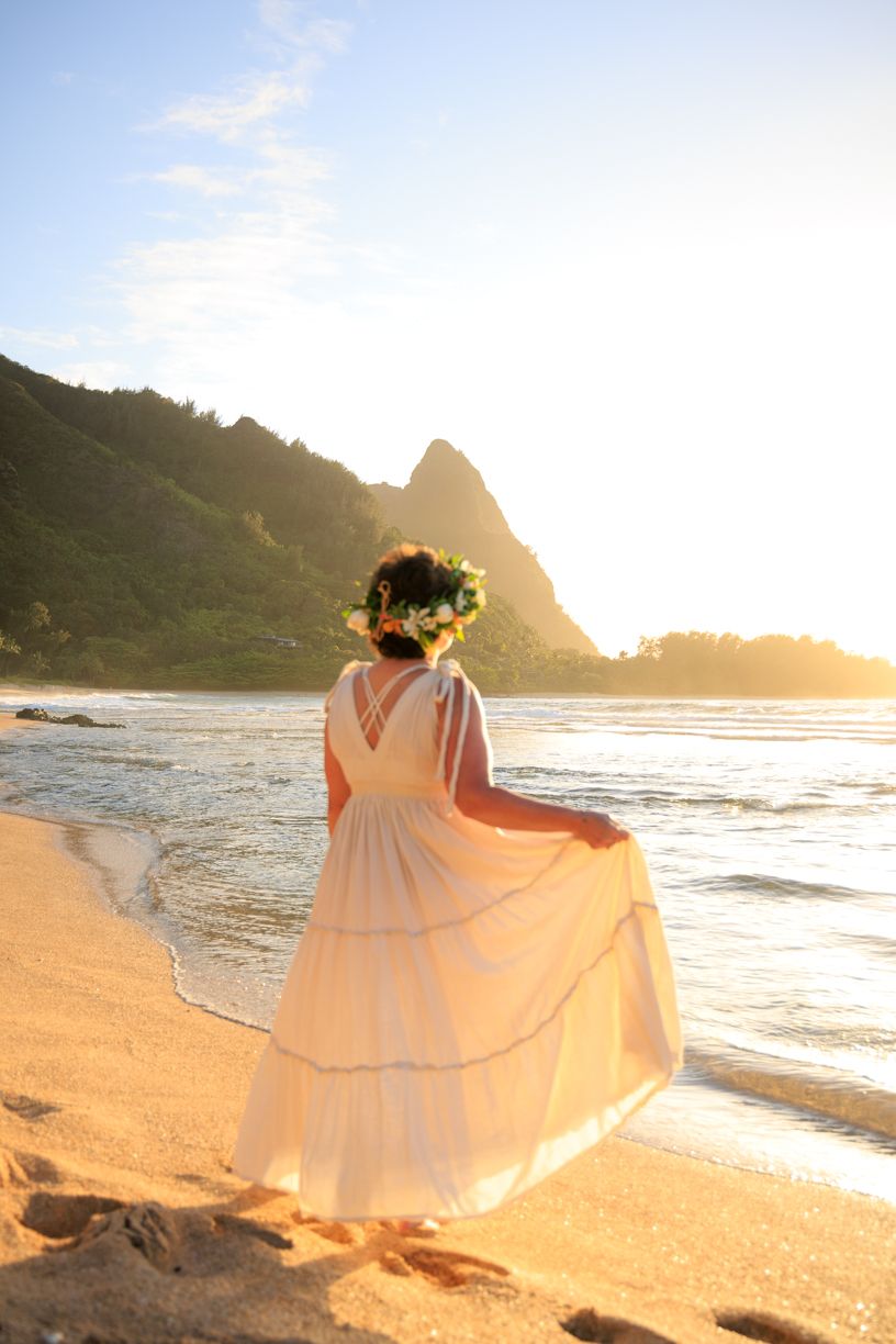 Flowing white dress catches sunset light on sandy beach with mountains in background.