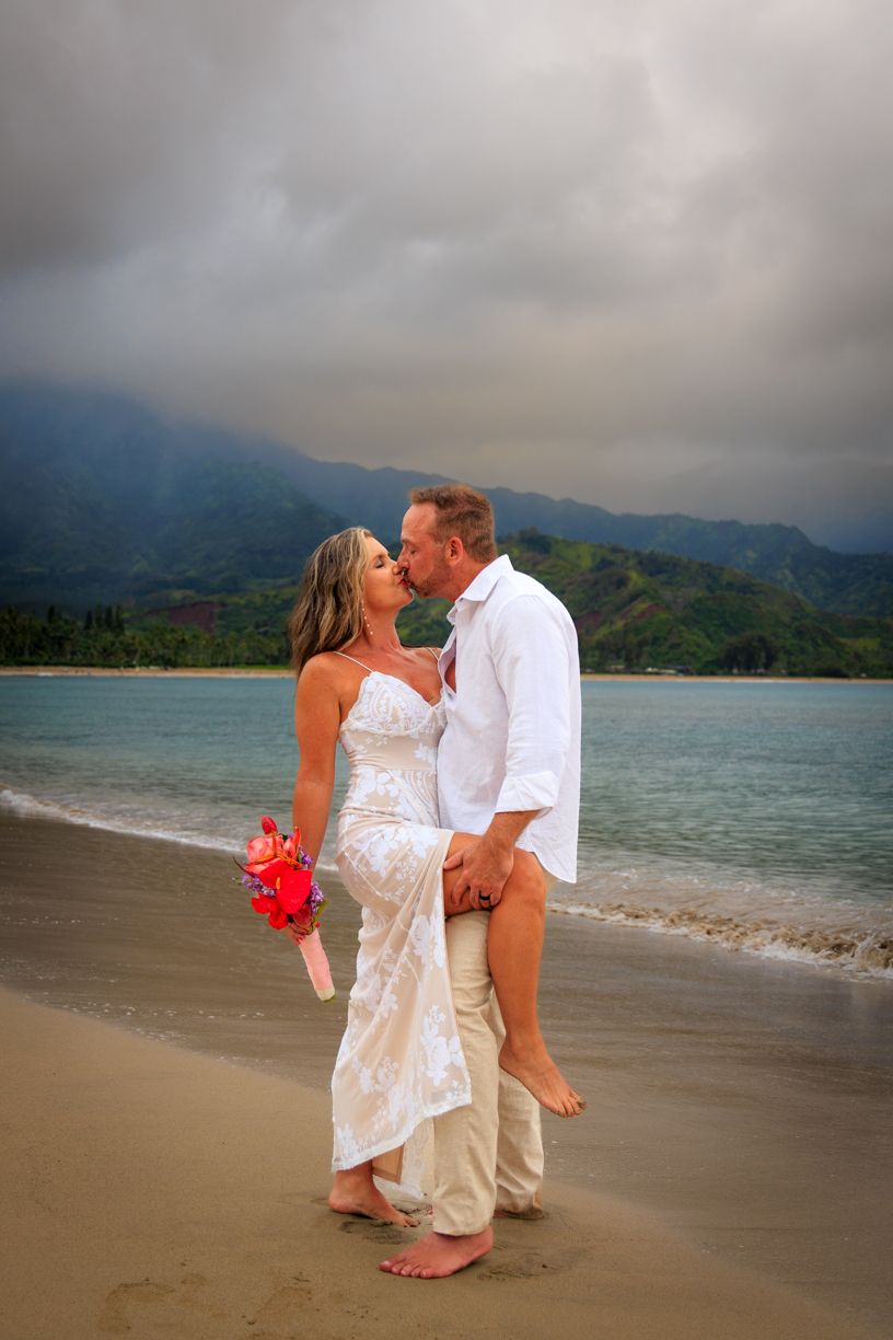 Romantic couple shares intimate moments on a tropical beach with mountains in the background.
