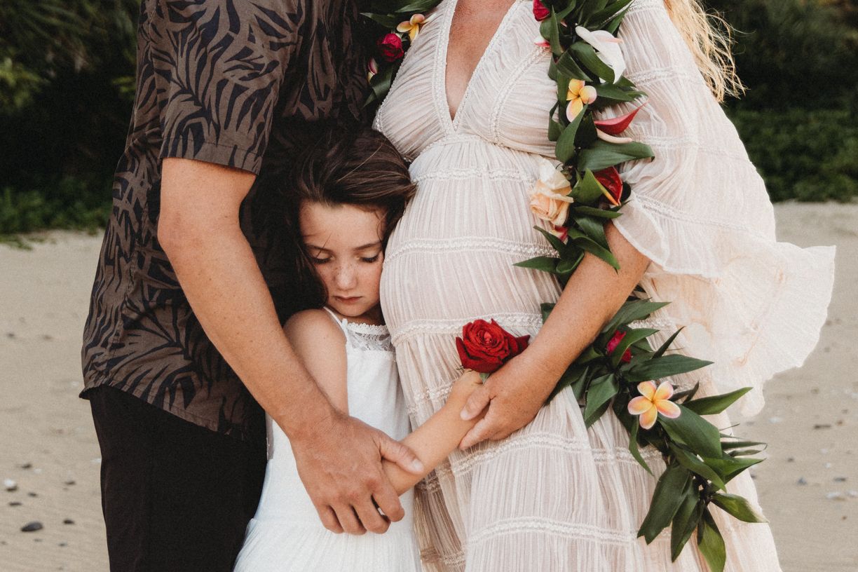 Intimate maternity photography details with flowing white dress and floral accents.