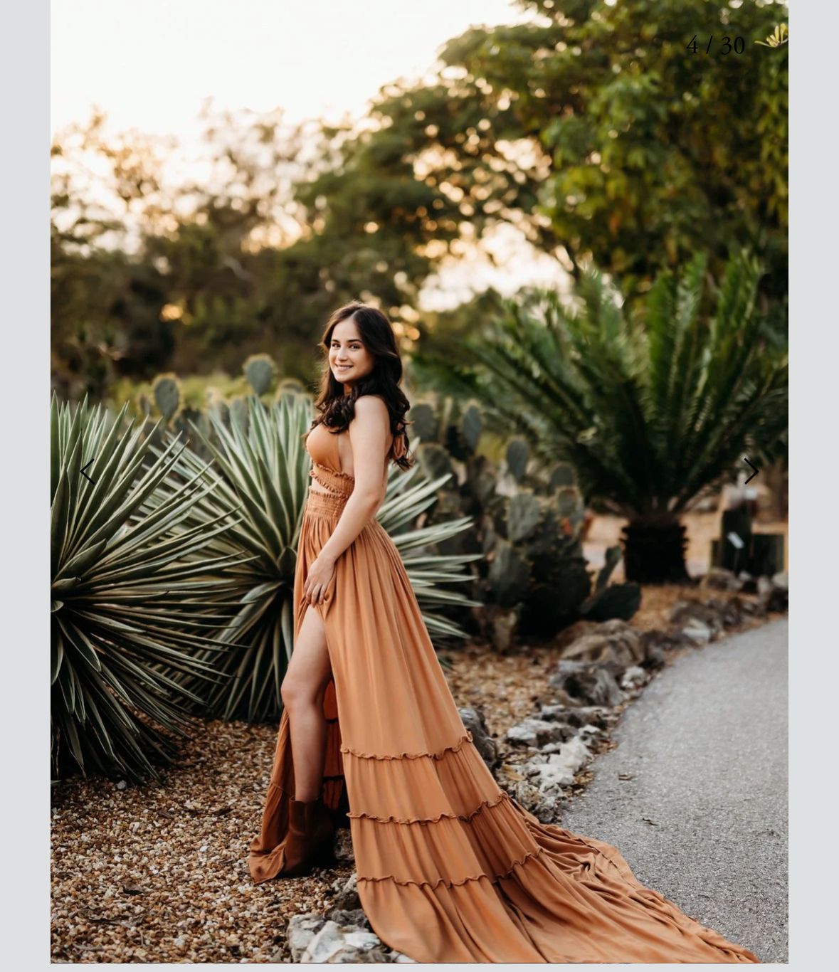 A person in a flowing rust-colored tiered dress poses gracefully in a desert garden setting with palm fronds.